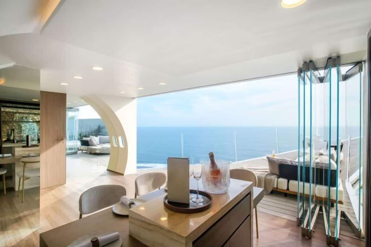 A modern interior with a dining area, a view of the ocean, and a balcony with seating.