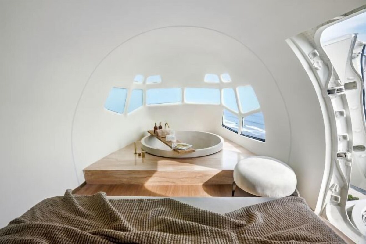 A modern, circular room with a central seating area, a wooden floor, and a view through a window.