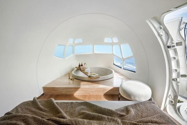 A modern, circular room with a central seating area, a wooden floor, and a view through a window. - Private Jet Villa Uluwatu (Bali)