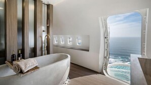 A modern bathroom with a large bathtub, a window with a view of the ocean, and a wooden panel wall. - Private Jet Villa Uluwatu (Bali)
