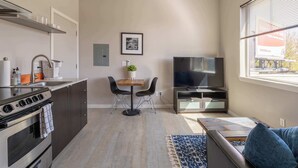 Ein kompakter Wohnbereich mit Küchenzeile, Essbereich, Fernseher und großem Fenster.