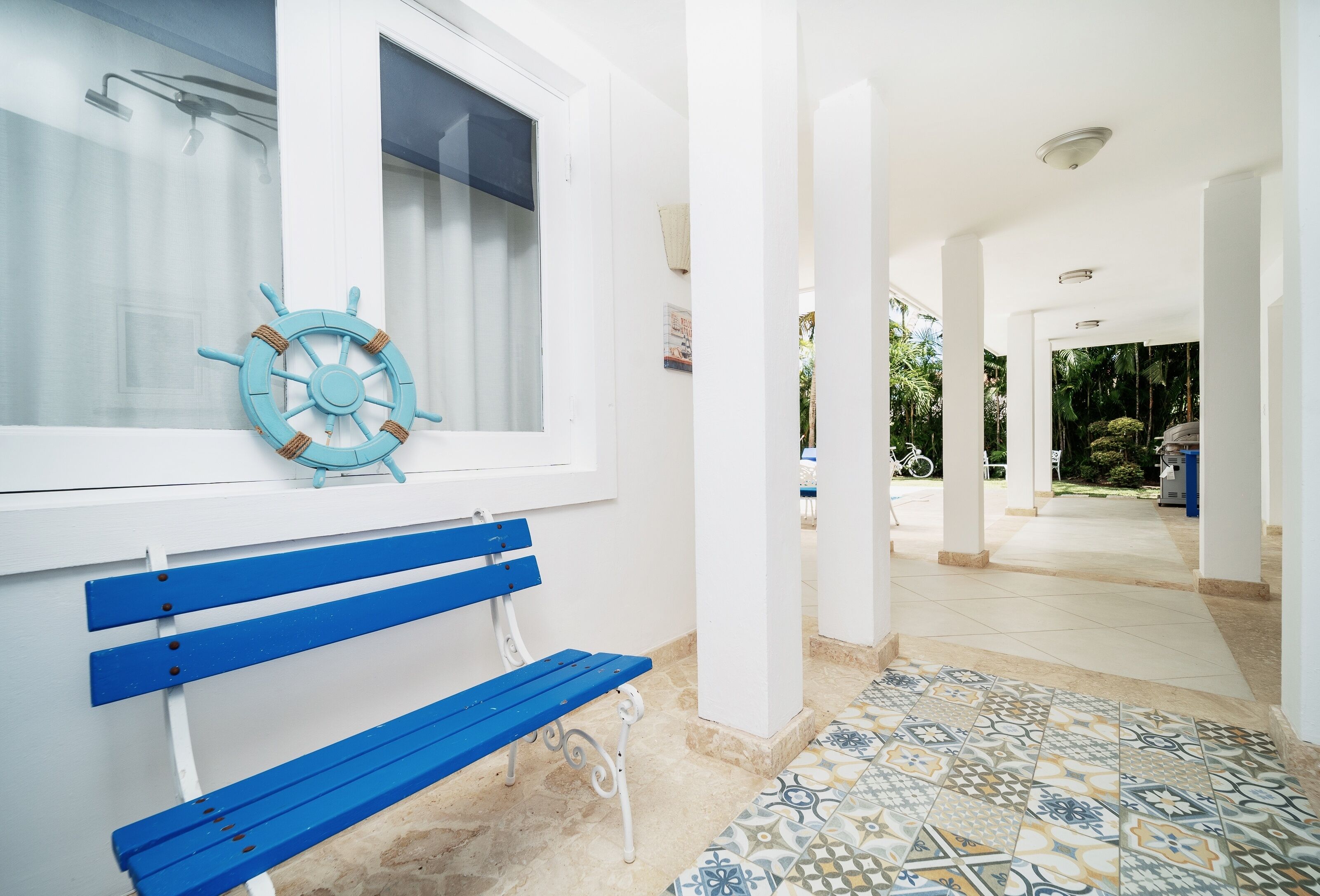 A white interior with a blue bench, a ship's wheel decoration, and a tiled floor.