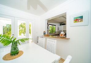 A bright kitchen with white cabinets, a dining table with chairs, a hanging plant, and a framed picture on the wall.