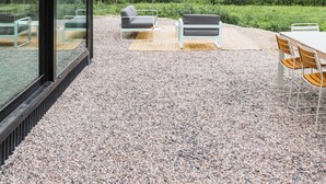 A modern outdoor patio with seating and a gravel floor.