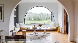 A cozy room with a large arched window, a round table, and a comfortable seating area.