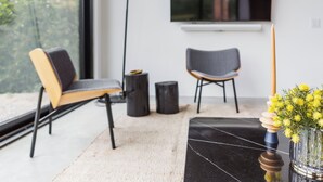 A modern living room with a large window, two chairs, a black coffee table, and a vase with yellow flowers.