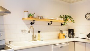 Une cuisine moderne avec des meubles blancs, un évier en acier inoxydable, un lave-vaisselle, une machine à café et un four à micro-ondes.