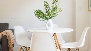 Un comedor con una mesa redonda, sillas blancas, una lámpara colgante y un tapiz tejido.