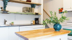 Cozinha com armários brancos, bancada de madeira, micro-ondas, cafeteira e uma planta decorativa num vaso azul.