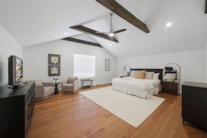 A bedroom with a bed, a desk, a chair, a television, and a ceiling fan.
