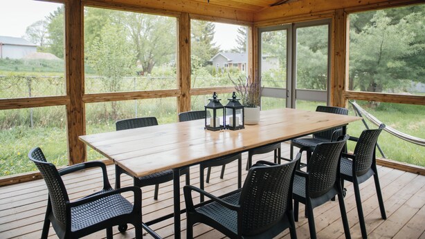 Una terraza de madera con una mesa, sillas y una hamaca.