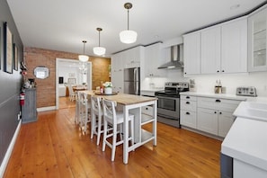 A modern kitchen with white cabinets, a wooden dining table, and a brick accent wall.