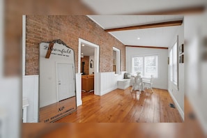 A room with wooden flooring, a brick wall, a white door, and a sign that reads 'Bloomfield Looks Good on You!'