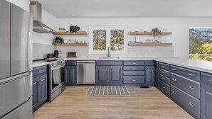 A modern kitchen with grey cabinets, stainless steel appliances, and wooden countertops. There are two windows providing natural light, and built-in shelves above the sink. - The Willows | 3 Bedrooms | 6 Guests | Heated Pool (Prince Edward)