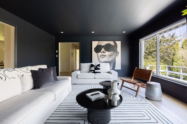 A modern living room with a white sofa, a black coffee table, and a large window with a view of trees.