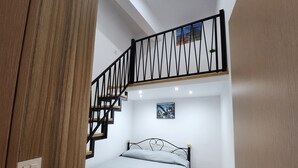 Quarto com cama, um quadro na parede, escada com corrimão e uma porta.