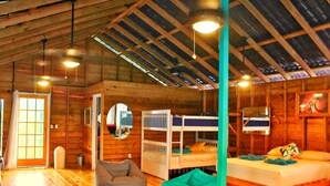 Una habitación acogedora de estilo cabaña, con paredes de madera y techo inclinado. Tiene literas, un sillón de saco y una mesita pequeña.