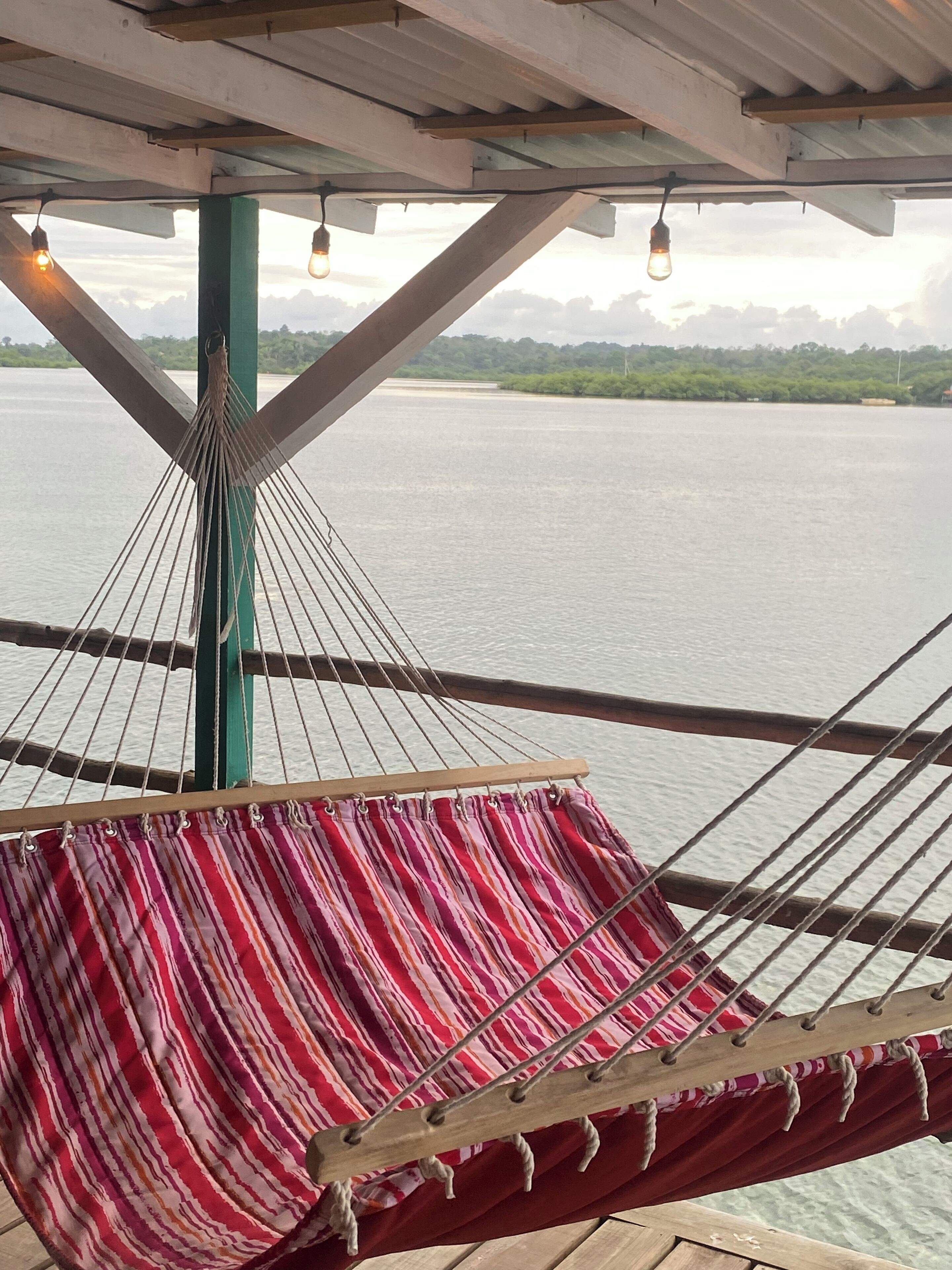 Una hamaca debajo de una estructura de madera con vista a un cuerpo de agua tranquilo y una costa distante.