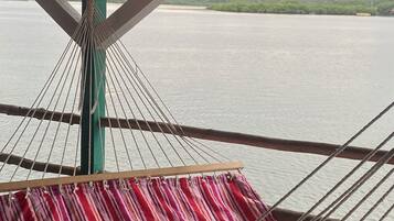 Una hamaca debajo de una estructura de madera con vista a un cuerpo de agua tranquilo y una costa distante.