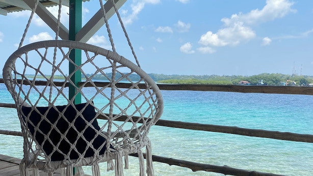 Terraza de madera con una silla colgante de macramé con vistas al mar azul y despejado.