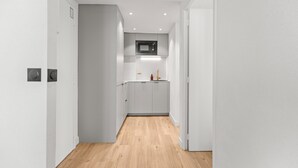 A narrow hallway with a wooden floor leading to a kitchen area with white cabinetry and a microwave. - Renovated Apartment Min. from Beach/Palais (Cannes)