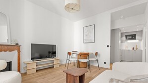 A modern living room with a flat-screen TV, wooden entertainment unit, round dining table with chairs, and a small wooden stool. - Renovated Apartment Min. from Beach/Palais (Cannes)