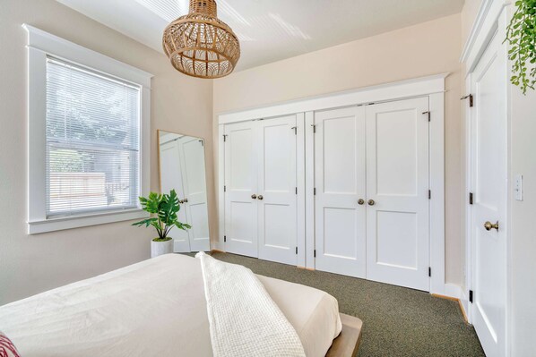A bedroom with a bed, a large wardrobe, a window with blinds, and a hanging light fixture.