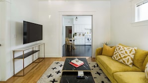 A modern living room with a flat-screen TV, a yellow sofa, and a coffee table with a book.
