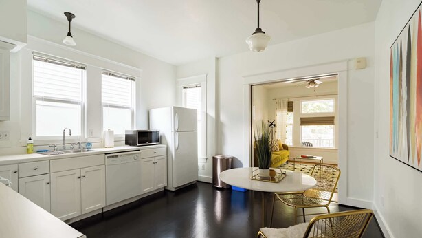 A modern kitchen with white cabinets, a stainless steel sink, and a round dining table with gold chairs.