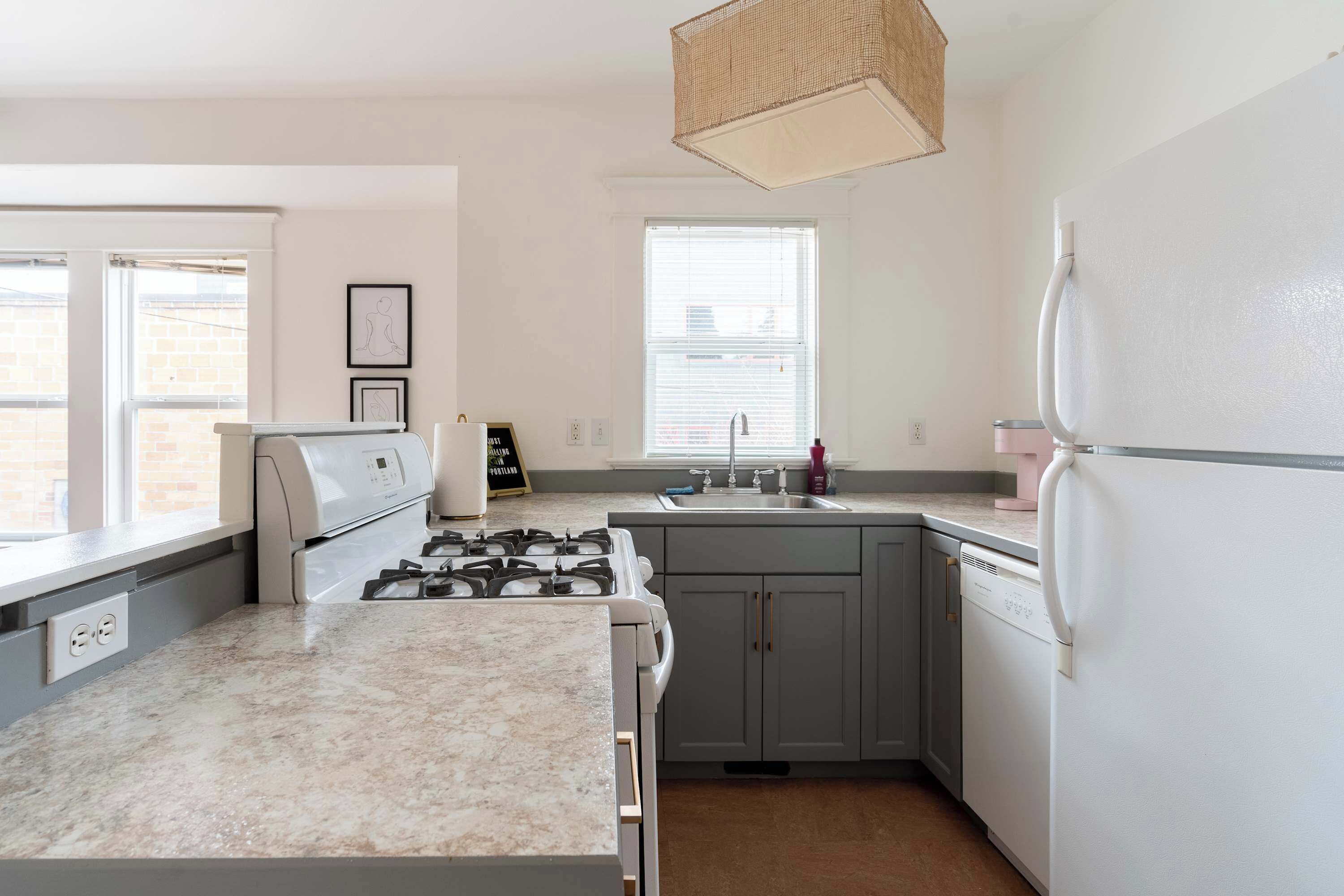 Una cocina moderna con estufa a gas, electrodomésticos blancos, gabinetes grises y un ventanal que proporciona luz natural.