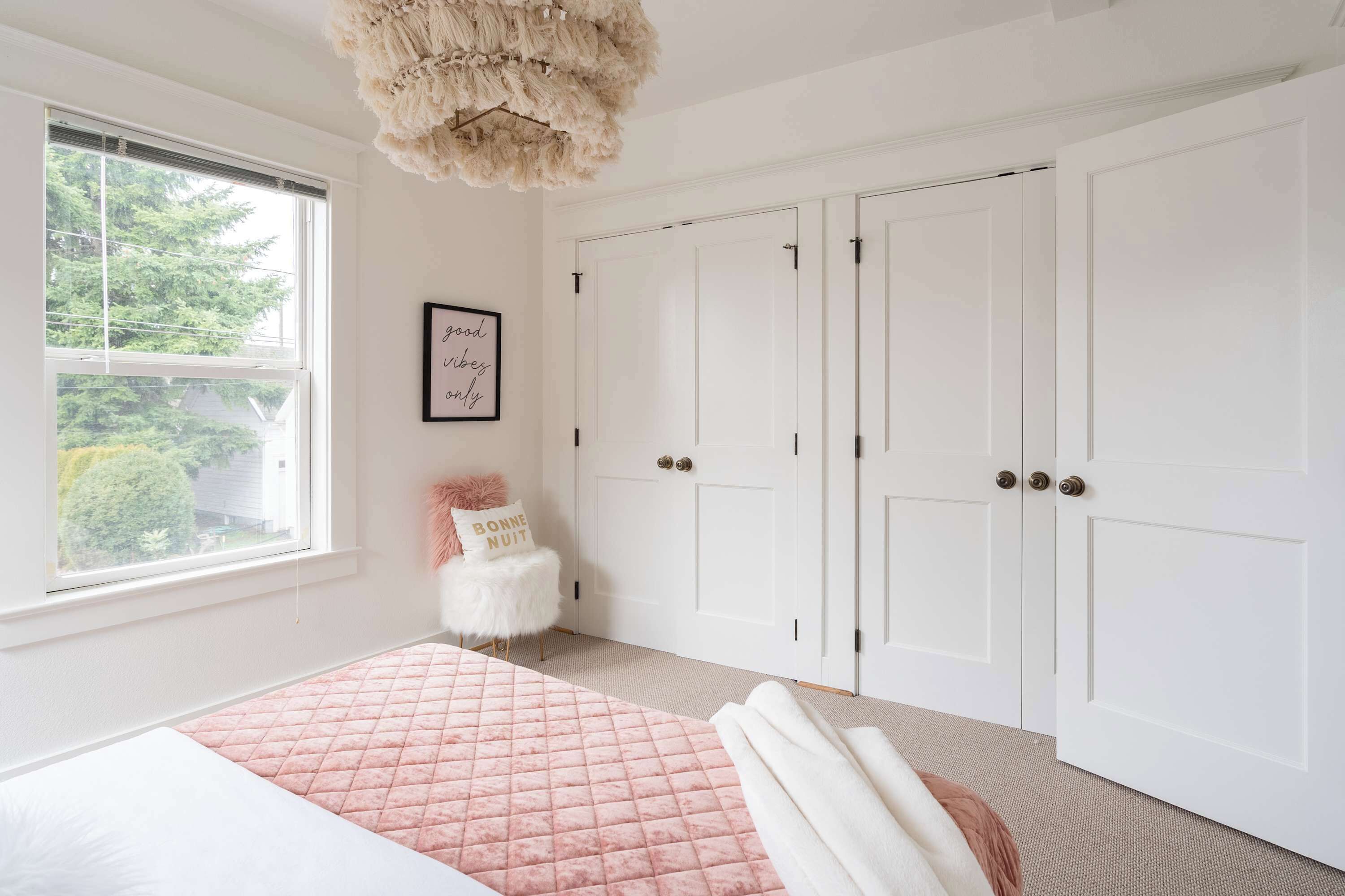 A bedroom with a bed, a window, a door, and a wall-mounted light fixture.