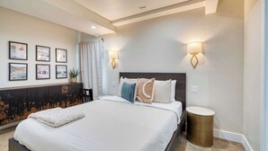 A bedroom with a large bed, a headboard, wall-mounted lights, and framed pictures on the wall.