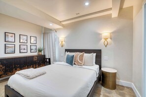 Een slaapkamer met een groot bed, een hoofdbord, wandlampen en ingekaderde foto's aan de muur.