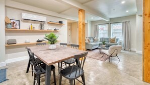 A modern living space with a dining area, a kitchen with built-in shelves, and a cozy seating area with a sofa and armchairs.
