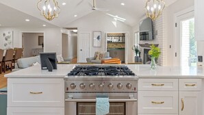 A modern kitchen with a central gas stove, white cabinetry, and pendant lighting. - Poolside Paradise-Kayaks/SUPs, Private Pool, Billiards, Foosball (Winchester)