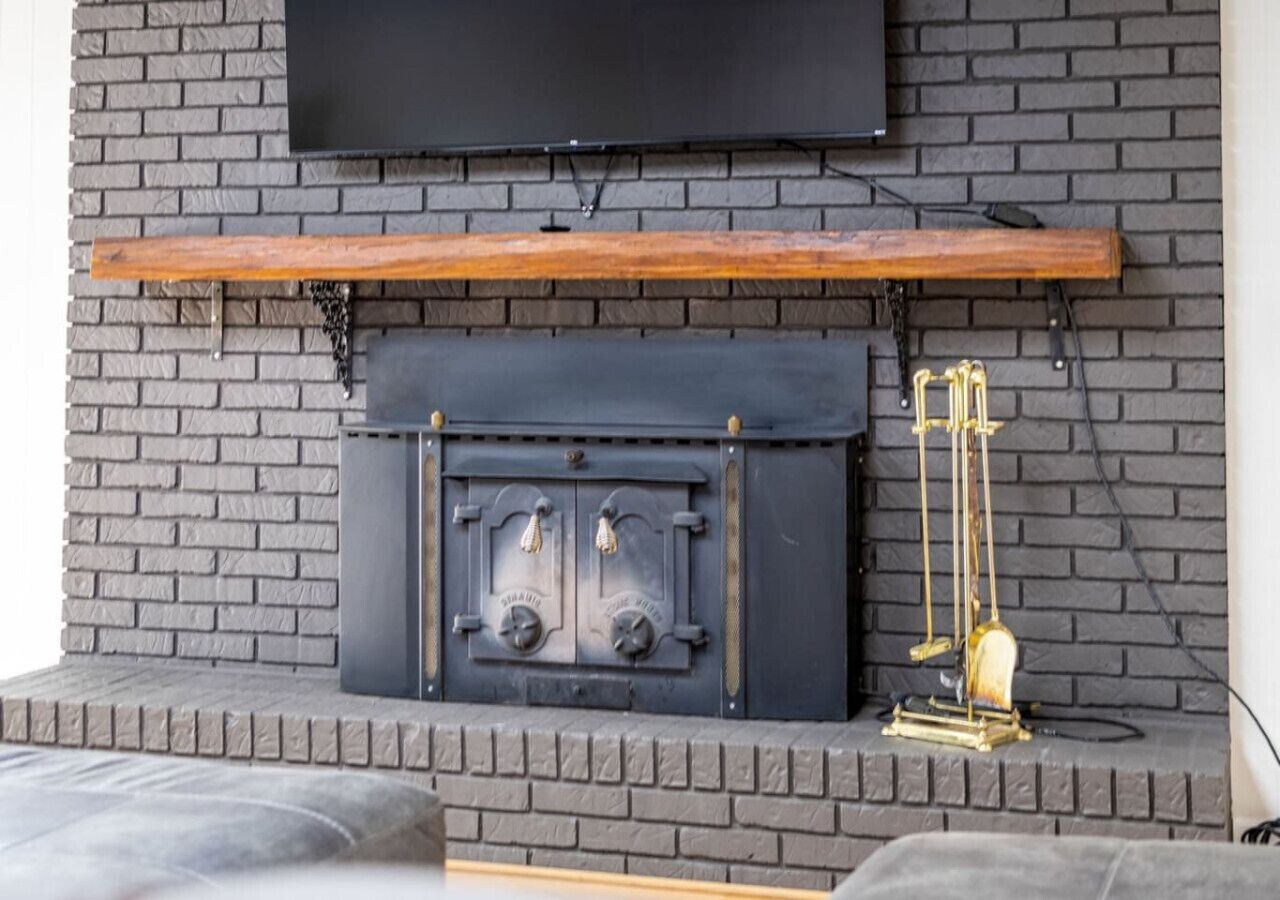 A fireplace with a black mantel and two brass handles, set in a brick wall with a mounted television above.