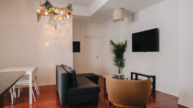 Un salon moderne comprenant un canapé, une table à manger, un téléviseur fixé au mur et un luminaire suspendu.