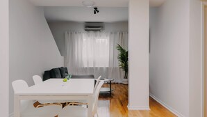 Ein modernes Wohnzimmer mit einem weißen Esstisch, weißen Stühlen, einem grauen Sofa und einem Blumentopf.