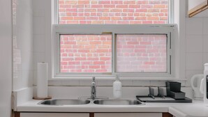 Eine Küche mit einem doppelten Spülbecken, einem Fenster mit Blick auf eine Ziegelwand und einer Kaffeemaschine auf der Arbeitsfläche.
