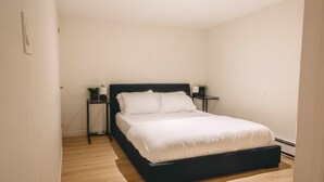 Quarto com estrutura de cama preta, roupa de cama branca e duas mesas de cabeceira com luminárias e pequenas plantas.