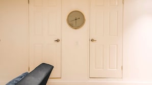 Um quarto com duas portas fechadas, um relógio de parede redondo e um banco.