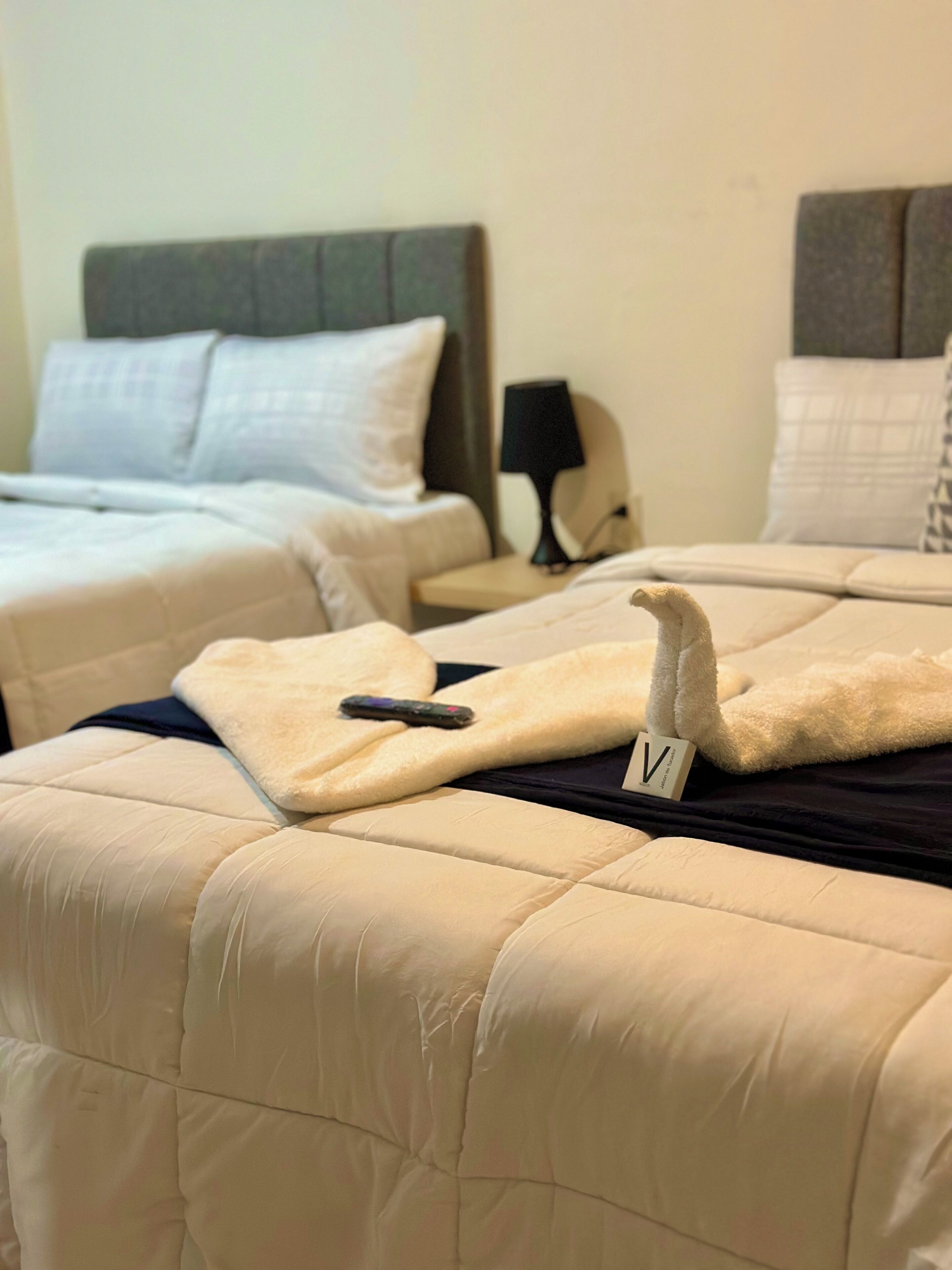 Une chambre d’hôtel avec deux lits, chacun recouvert d’une courtepointe beige matelassée et muni d’une télécommande sur l’un des lits.