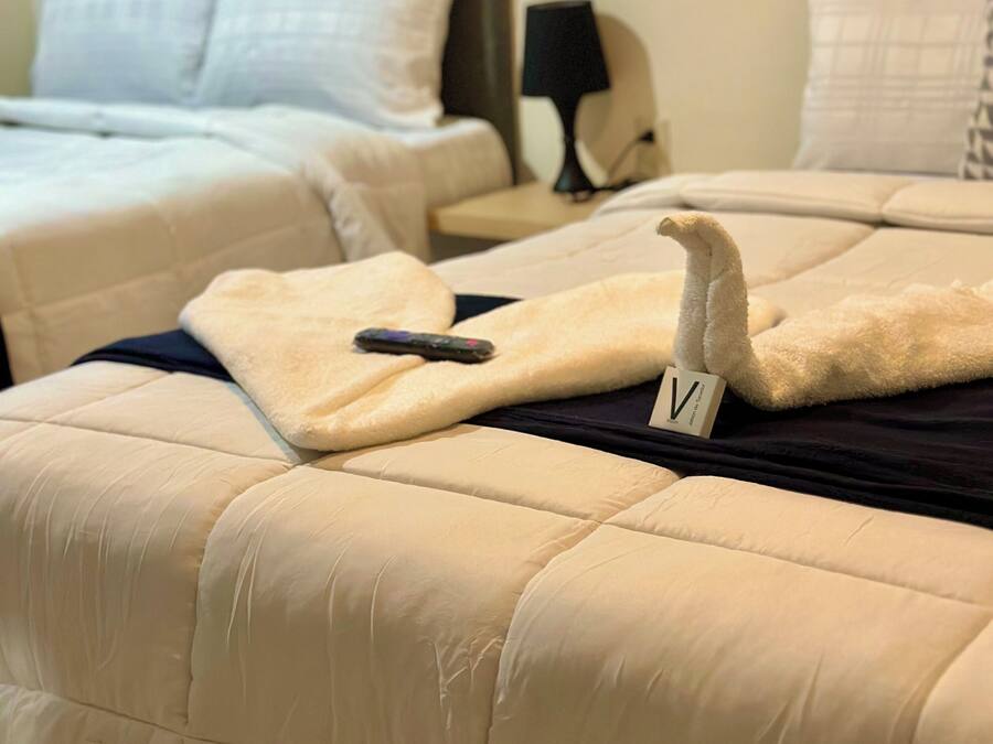 Une chambre d’hôtel avec deux lits, chacun recouvert d’une courtepointe beige matelassée et muni d’une télécommande sur l’un des lits.