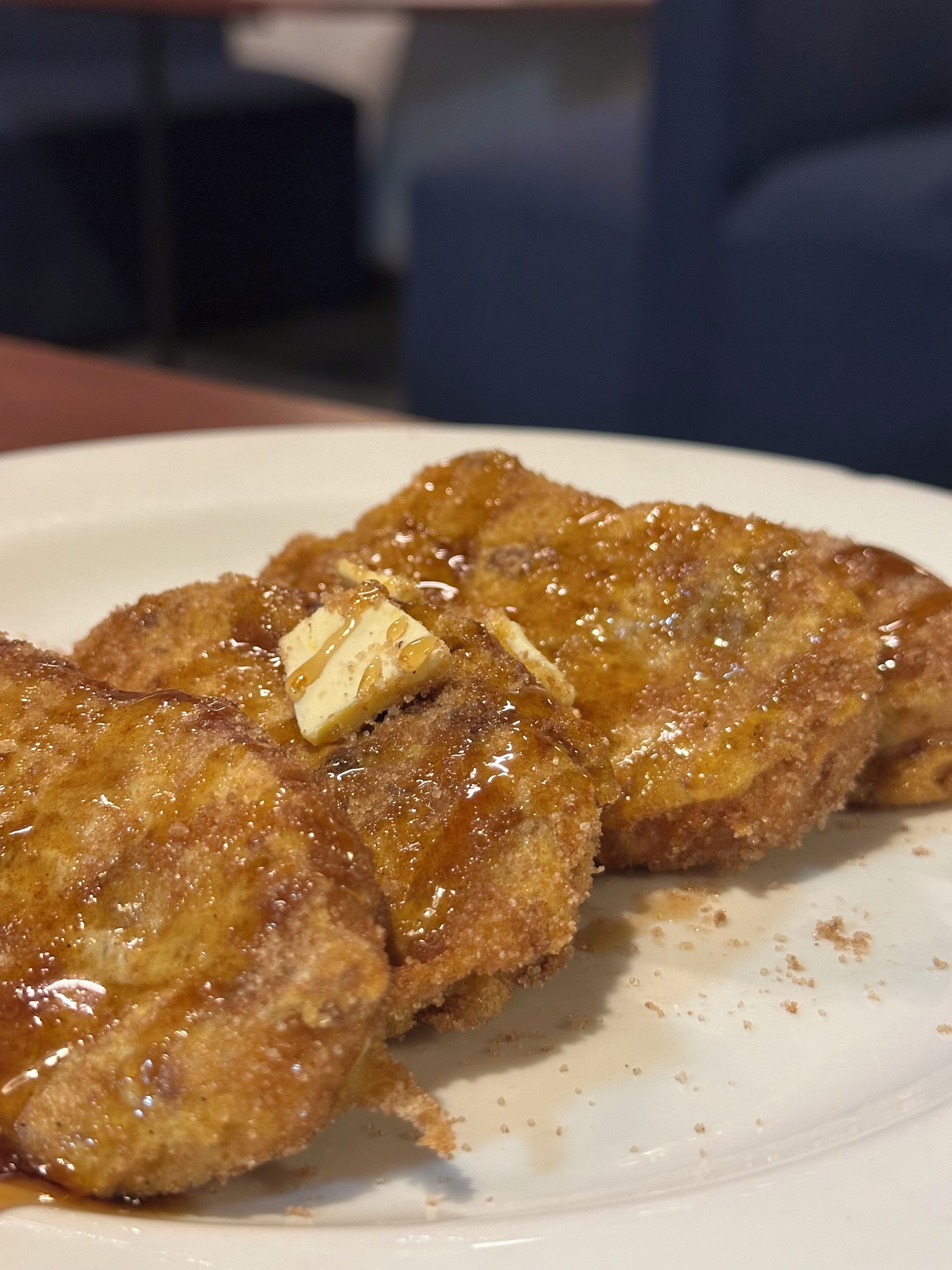 A plate with a piece of breaded and fried food, possibly a sandwich or chicken cutlet, with a pat of butter melting on top.