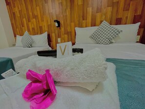 A hotel room with a wooden headboard, a bed with white bedding, a V-shaped sign, and a teal blanket.