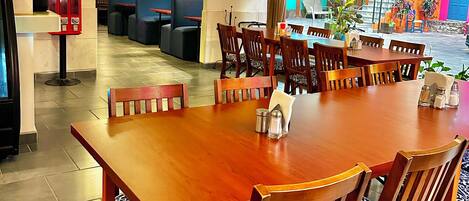 Un comedor con mesa y sillas de madera, una alarma contra incendios roja y vistas a un área exterior colorida con escaleras.