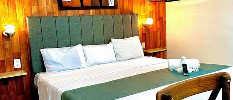 A neatly made bed with a green headboard, a wooden wall panel, and a wall-mounted light fixture.