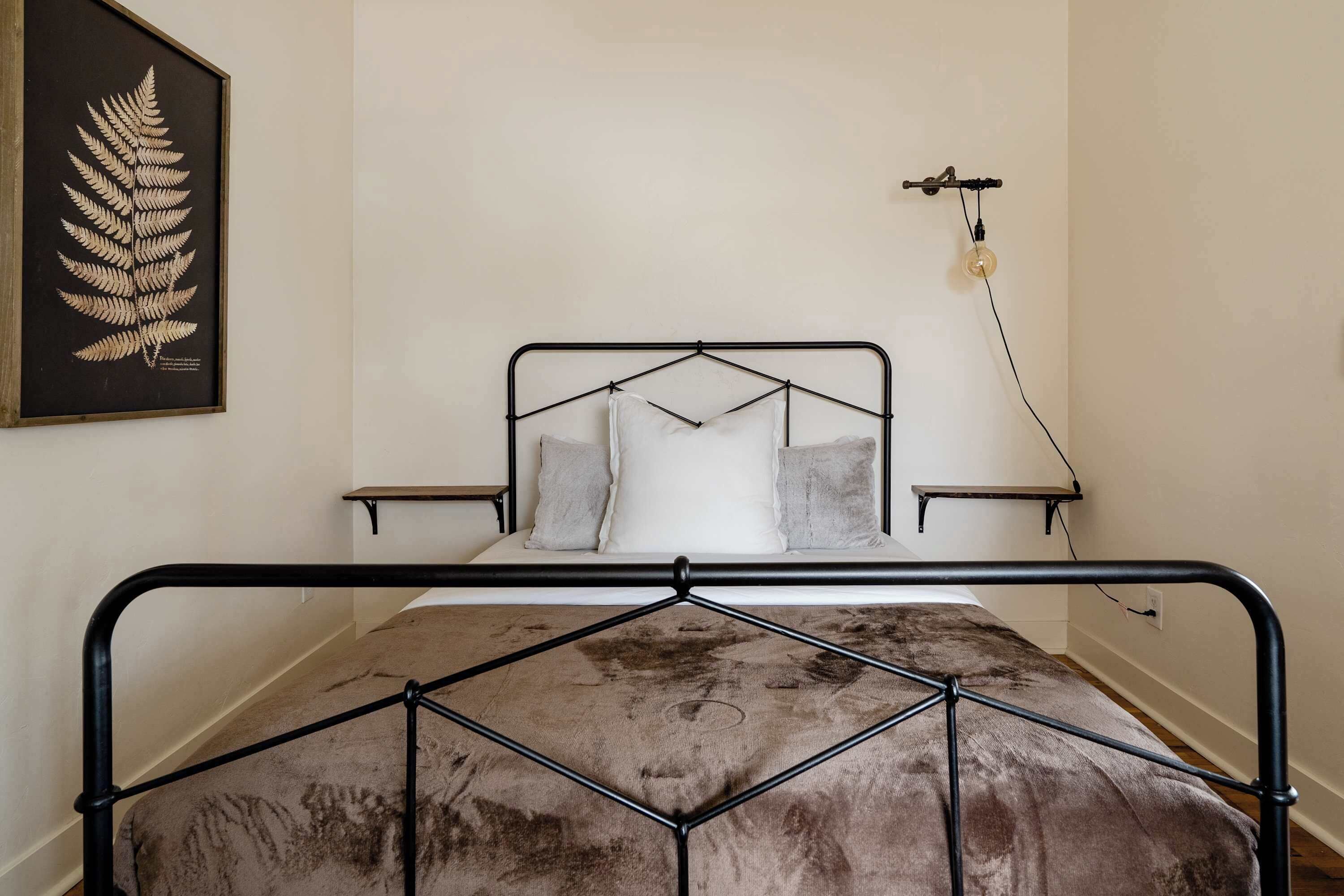 Ein Bett mit Metallgestell, einer braunen Decke und Kissen an einer weißen Wand.