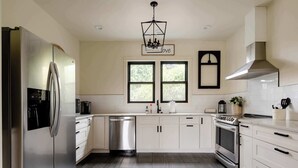A modern kitchen with stainless steel appliances, white cabinetry, and a large window providing natural light. - 1920s Farmhouse | 4BR/2BA | Foodie District (Portland)