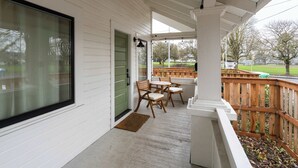 A covered porch with a wooden deck, a green door, and a bench. - 1920s Farmhouse | 4BR/2BA | Foodie District (Portland)